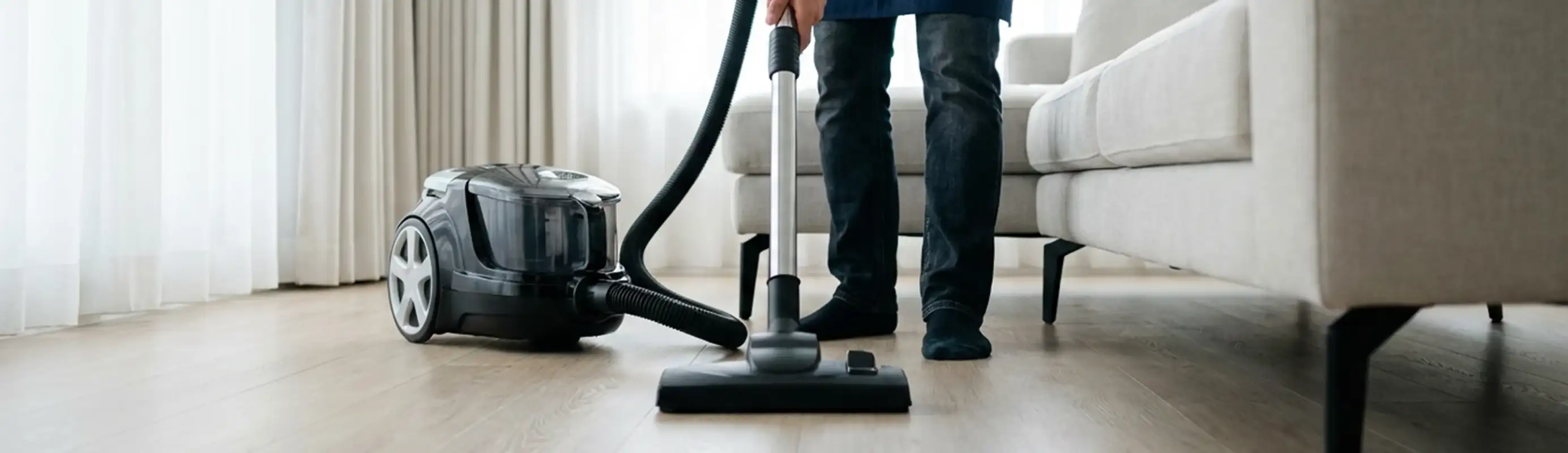 Professional house cleaner vacuuming a living room floor with a canister vacuum cleaner, Anchorage, AK.