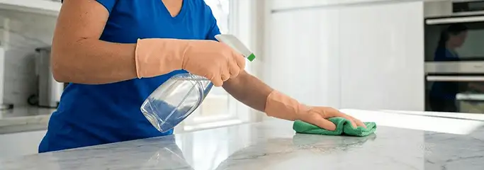 Maid service worker spraying and wiping a kitchen countertop with a microfiber cloth for sanitizing, Anchorage, AK.