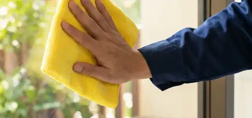 House cleaner wiping a glass window with a yellow microfiber cloth for streak-free cleaning, Anchorage, AK.